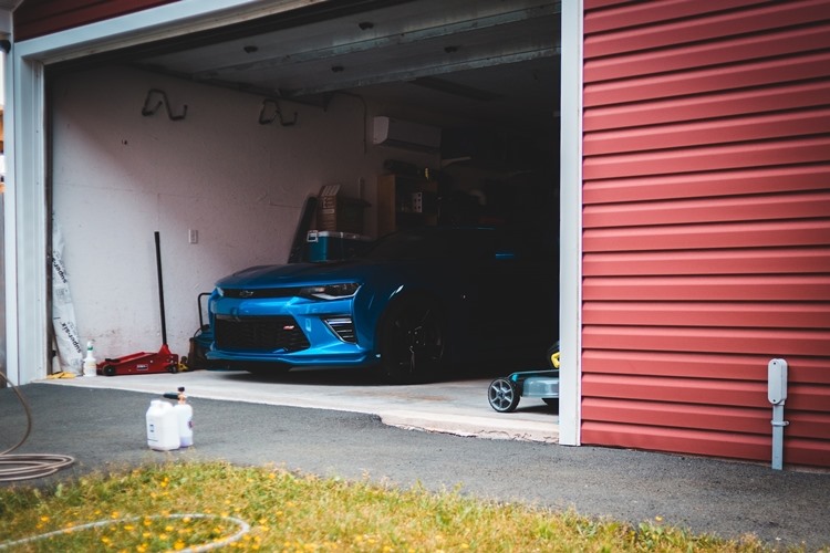 Blue sportscar in garage with red siding, white trim and open overhead door