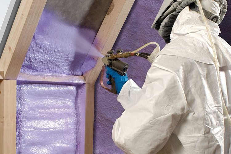 Technican in hazmat suit spraying insulation around wall studs