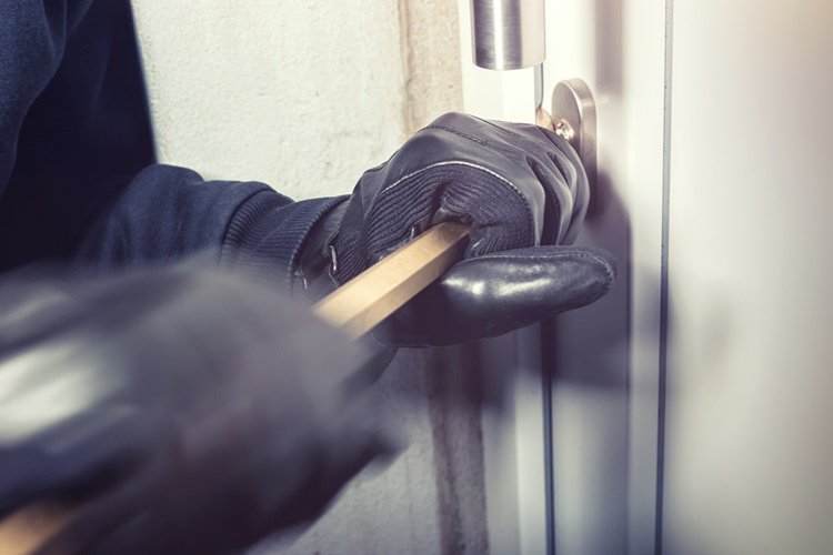Robber in black leather gloves prying open side door of residential garage with crowbar