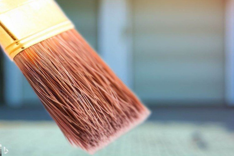 Paintbrush in hand viewed close-up with two car residential garage in background