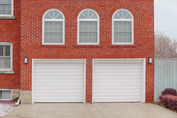 Two-story house with red brick exterior and two white paneled garage doors
