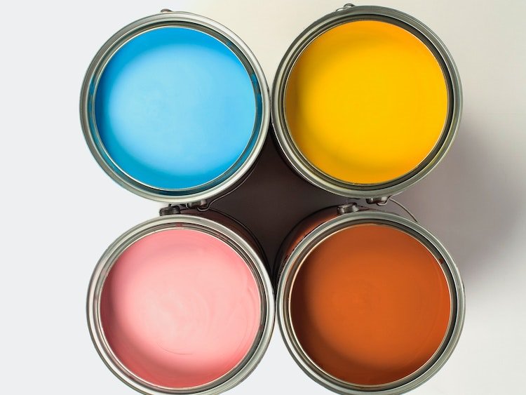 Aerial view of four gallon-sized paint cans containing blue, yellow, pink and rust-colored paint