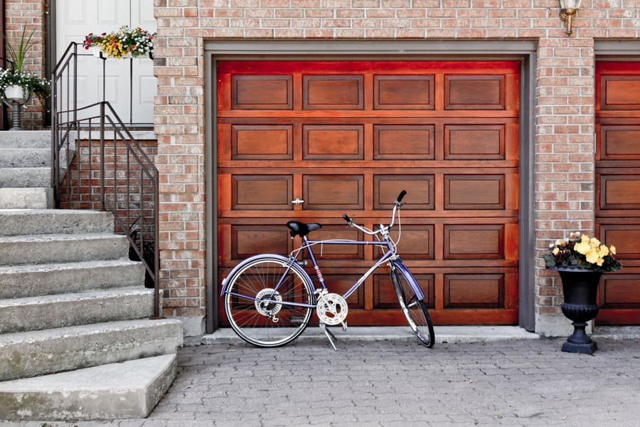 Single paneled mahogany wood garage door closed near purple bicycle, cement staircase and driveway
