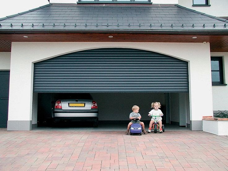 Green garage door halfway open with silver sedan inside and two toddlers playing in driveway